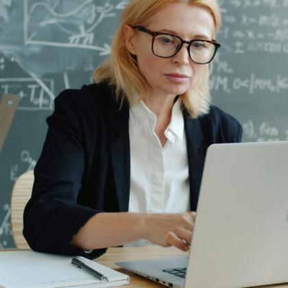 Educator looking at a computer with a blackboard of text behind her.